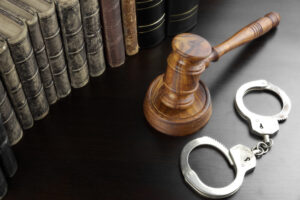 Judges Gavel, Handcuffs And Old Law Book On The Black Wooden Table Background In The Back Light. Overhead View. Lawsuit or Bail Or Arrest Concept